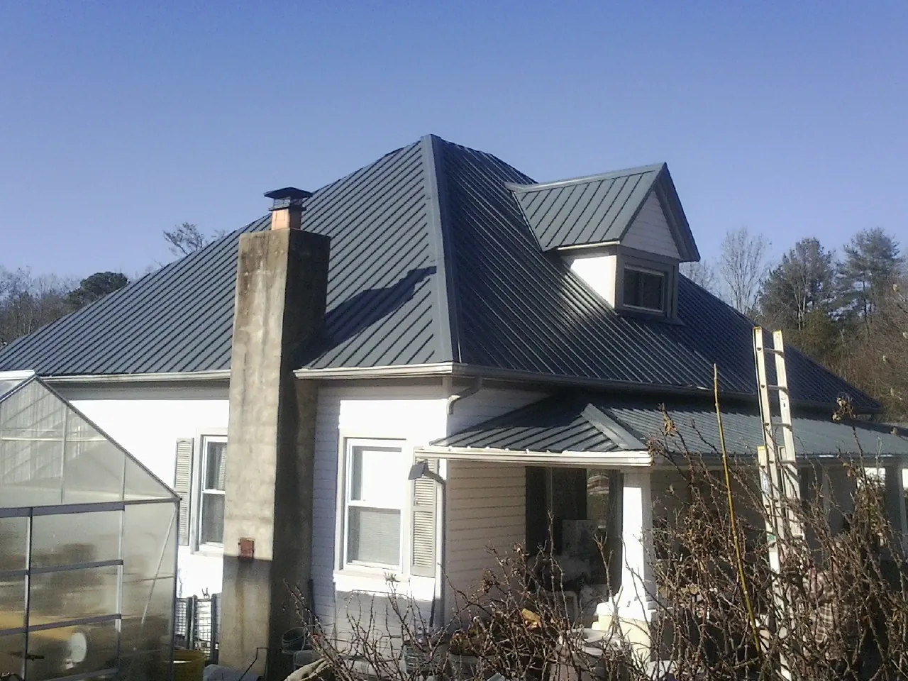 Dark blue standing seam metal roof on a white farmhouse with dormer — Slate & Tile Roof Repair by Roofing Brothers in Shorter