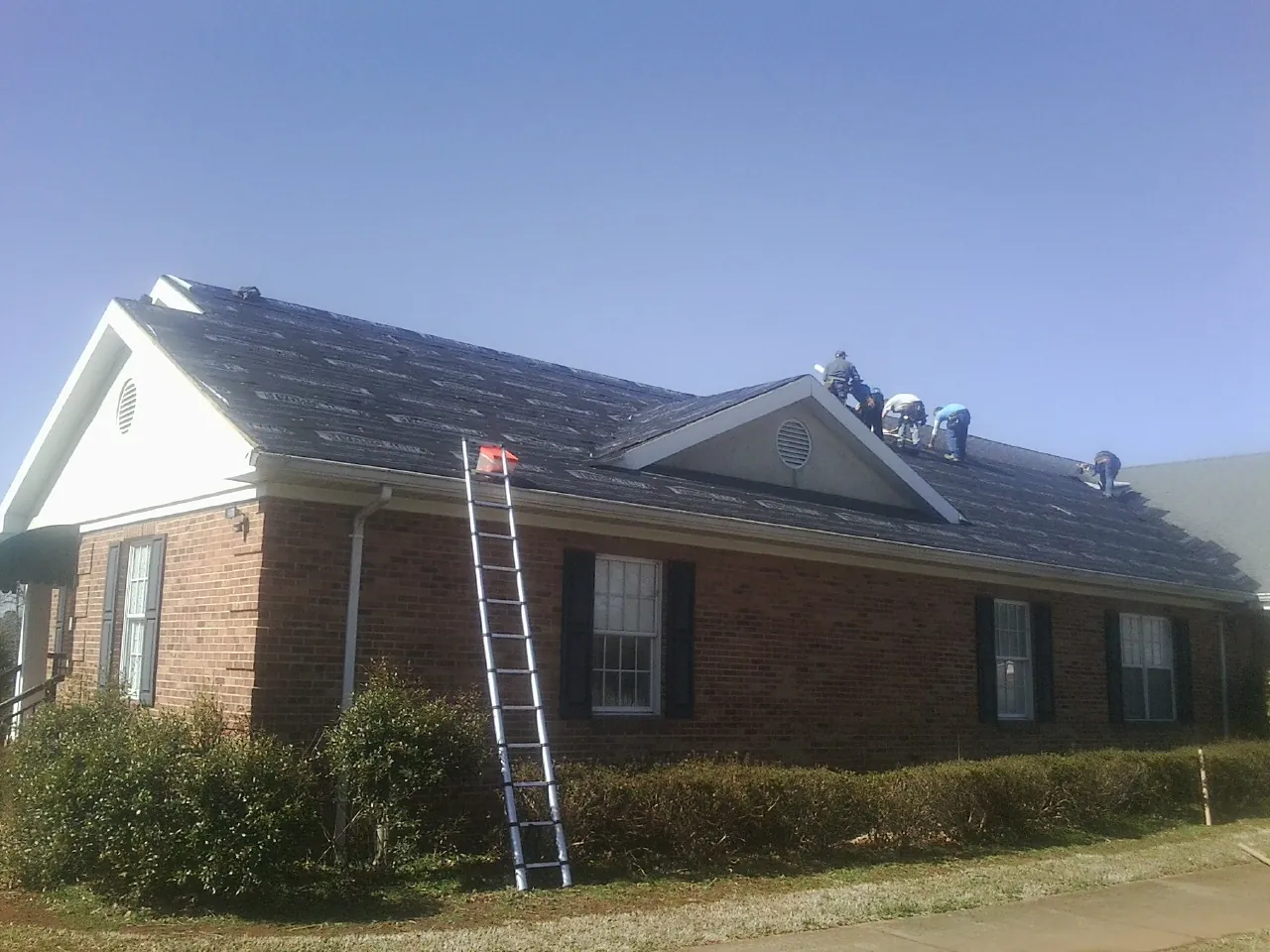 Crew tearing shingles off a brick ranch roof with a ladder set — Metal Roof Repair work by our crew in Shorter