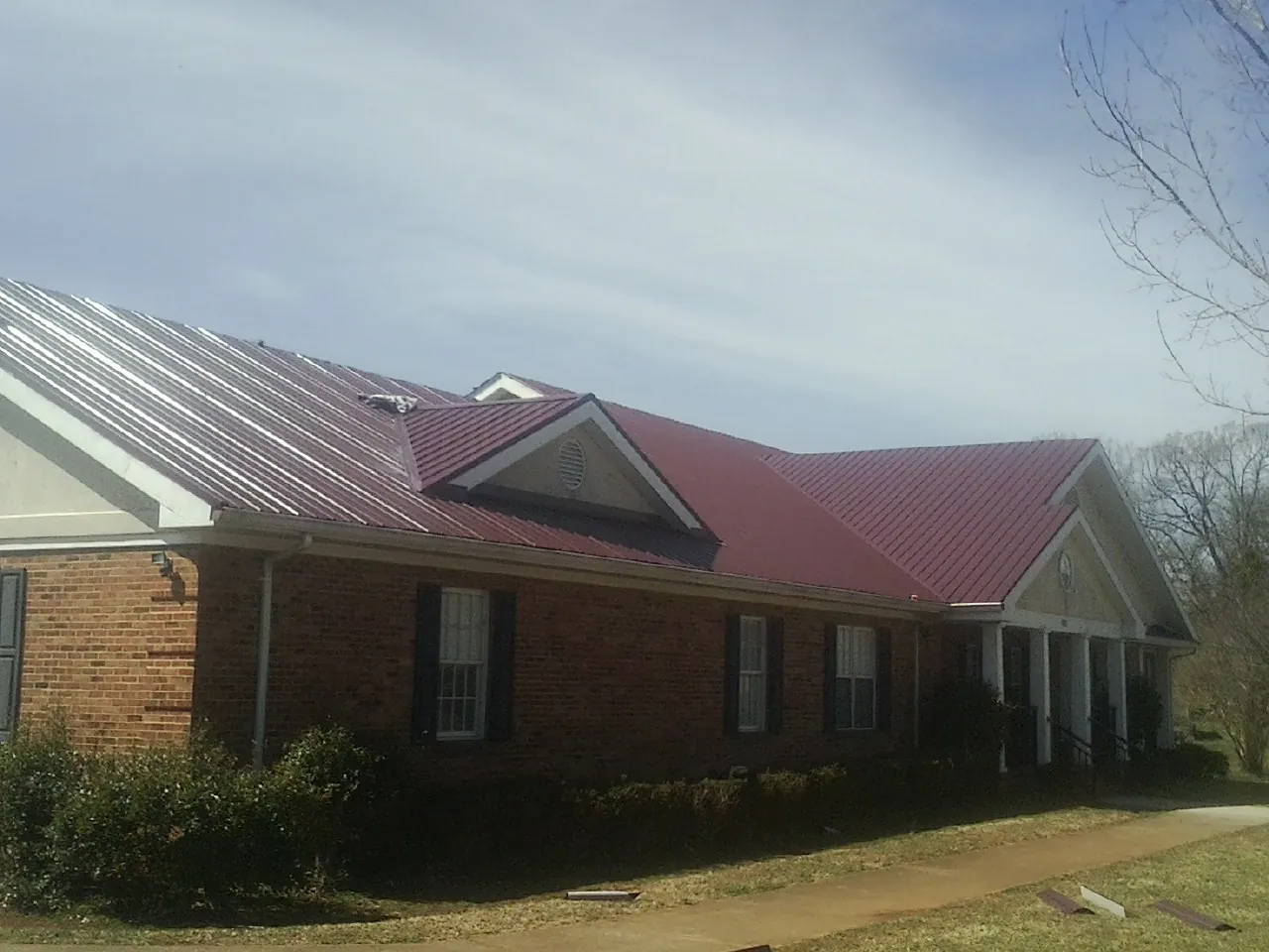 Red metal roof with gabled entries on a long brick building, from a Hail Damage Roof Repair job in Shorter
