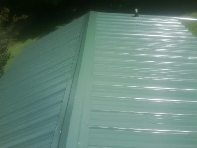 New green metal panels meeting at the ridge of a roof — Flat Roof Repair work by our crew in Shorter