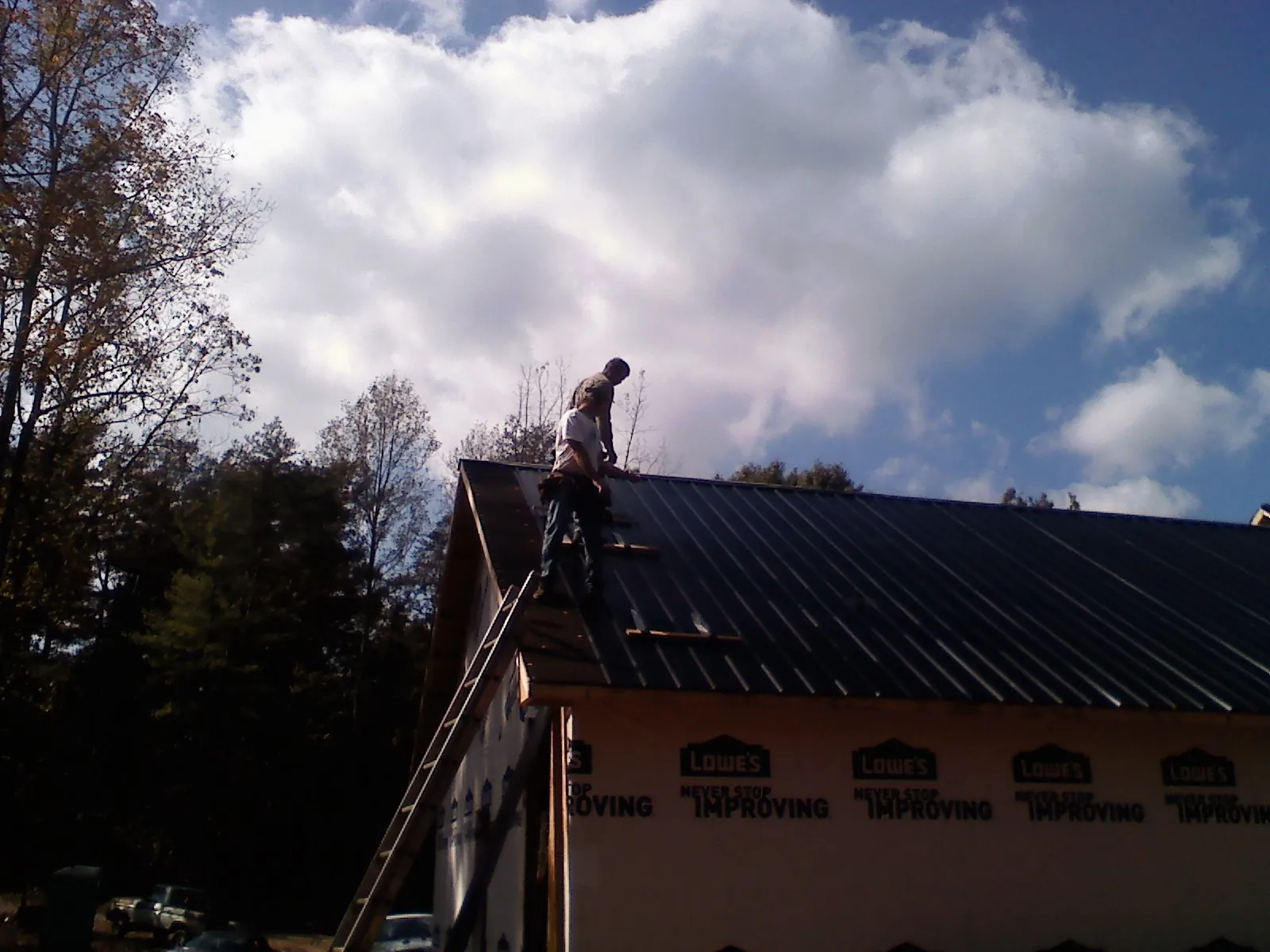 Roofer fastening dark metal panels high against a cloudy sky, from a Roof Inspection job in Shorter