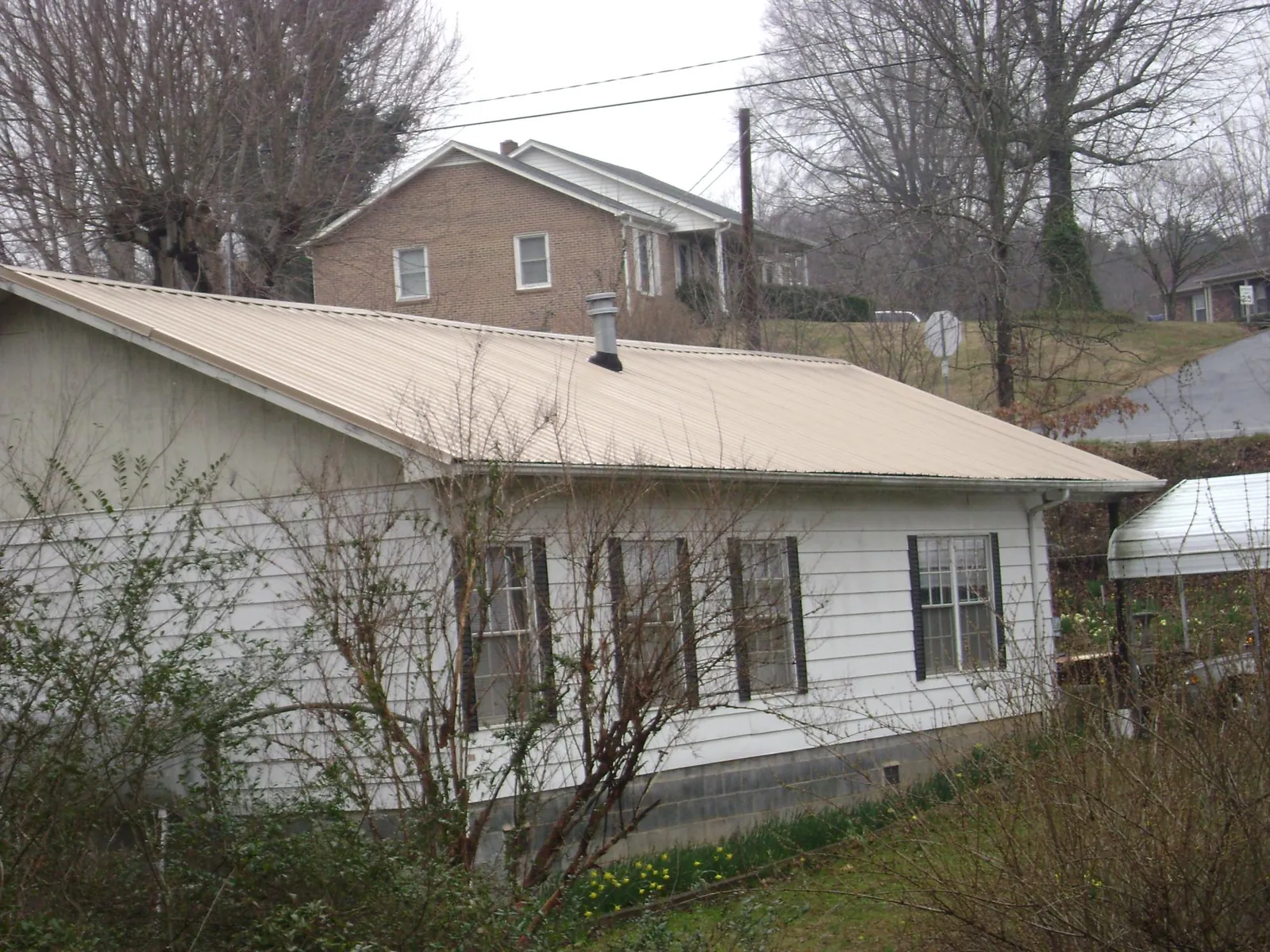 Tan metal roof on a white sided house set into a hillside — Commercial Roofing by Roofing Brothers in Shorter